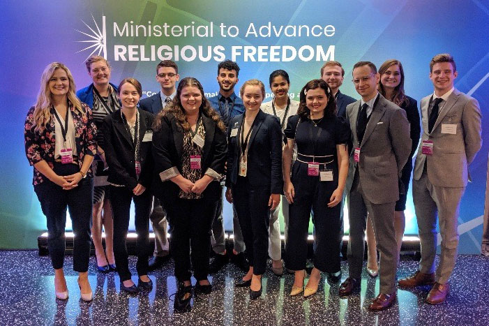 Sam Goldman with undergraduate students in front of a sign, Ministerial to Advance Religious Freedom