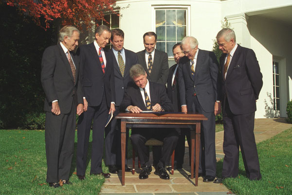 President Bill Clinton sitting at a desk signing the Religious Freedom Restoration Act with several men in black suits standing around him